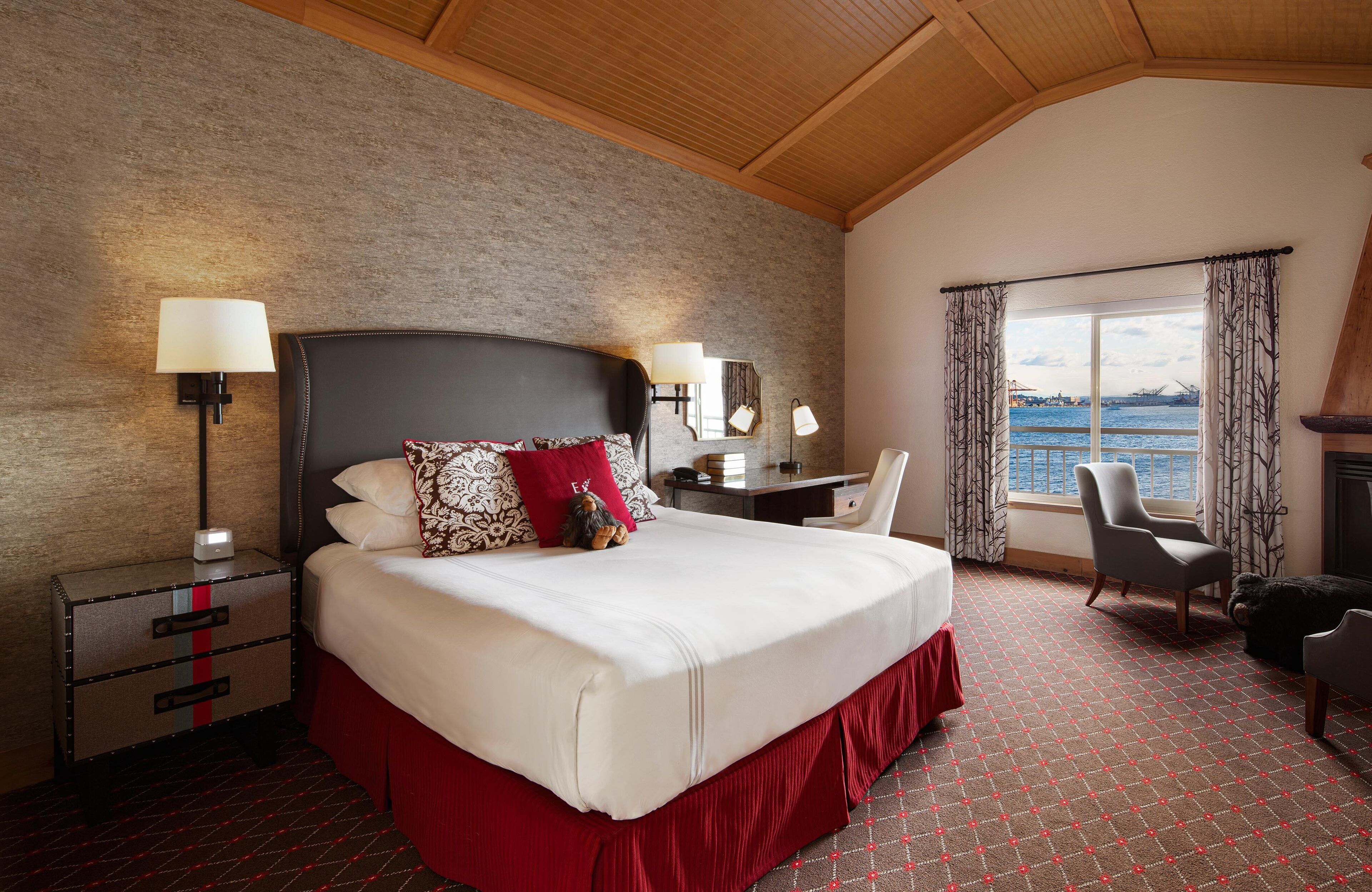 A hotel room with a large bed, a desk, a chair, a lamp, and a view of the sea.