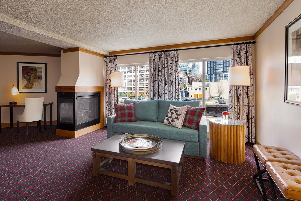 A hotel room with a sofa, a coffee table, a TV, a fireplace, and a view of the city.