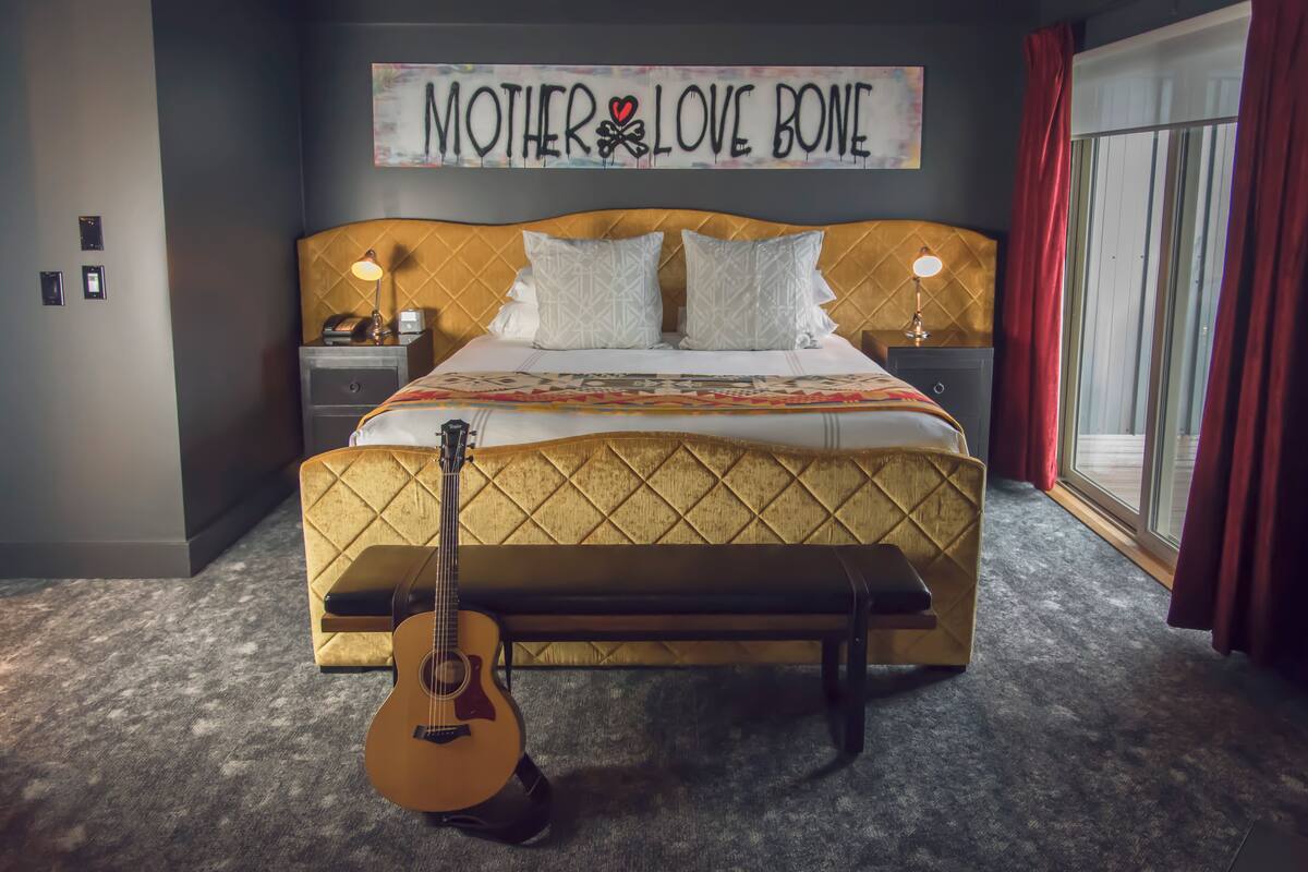 A bedroom with a bed, a guitar, a bench, and a wall sign.