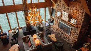 Un interior acogedor con chimenea de piedra, asientos cómodos y amplios ventanales con vistas al agua.