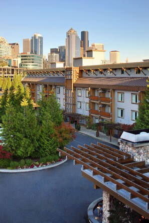 A multi-story hotel with balconies, a parking area, and a city skyline in the background.