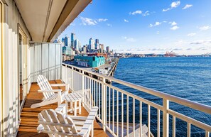 A balcony with white chairs and a view of a city skyline and water.
