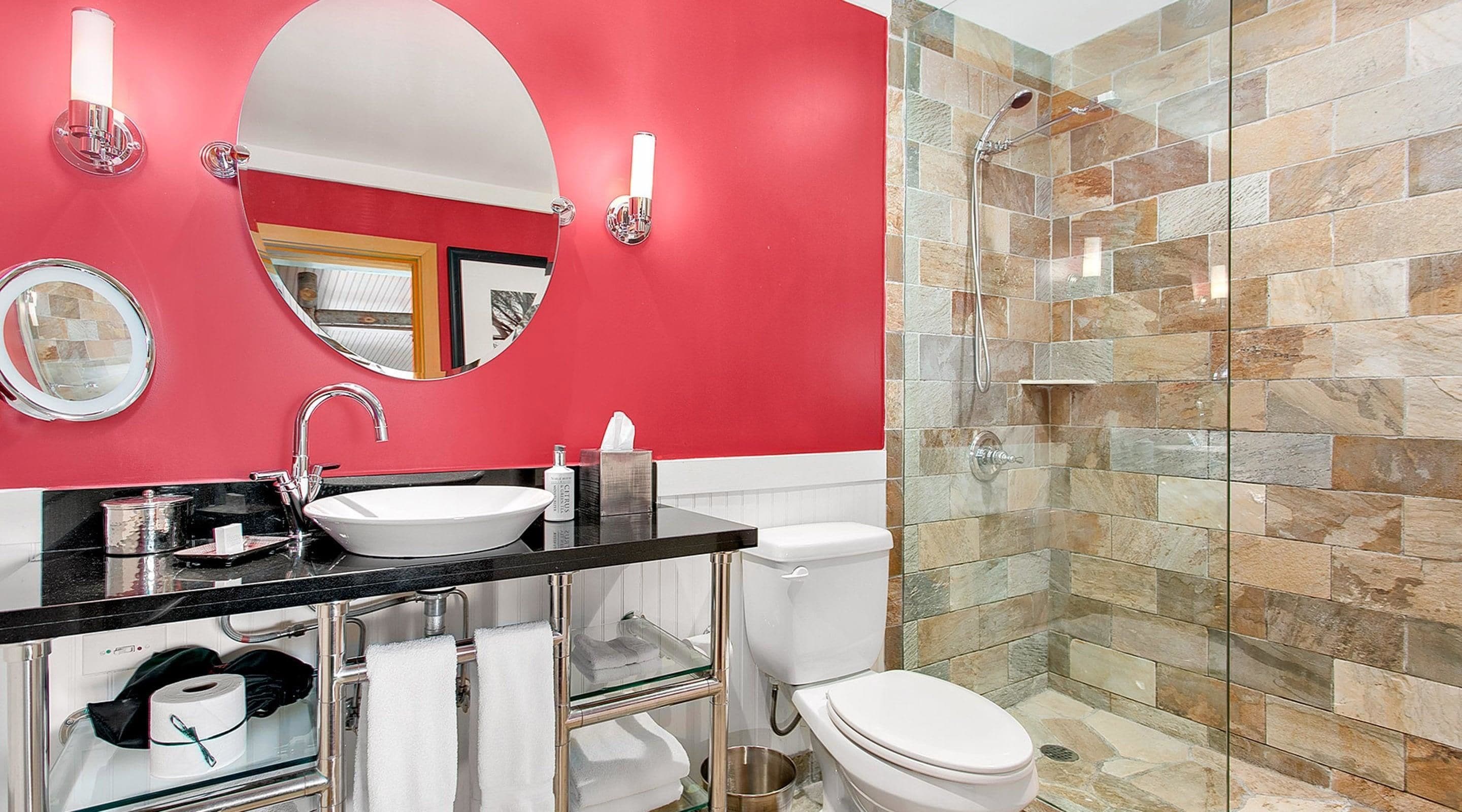 A modern bathroom with a red accent wall, a white sink, a glass shower enclosure, and a toilet.