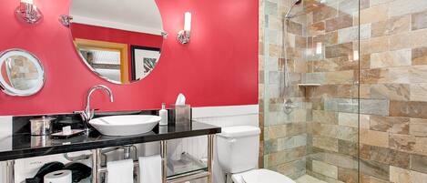 A modern bathroom with a red accent wall, a white sink, a glass shower enclosure, and a toilet.
