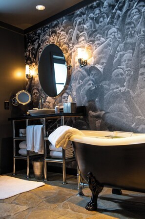 A bathroom with a freestanding bathtub, a round mirror, a sink with a towel rack, and a wall-mounted light fixture.