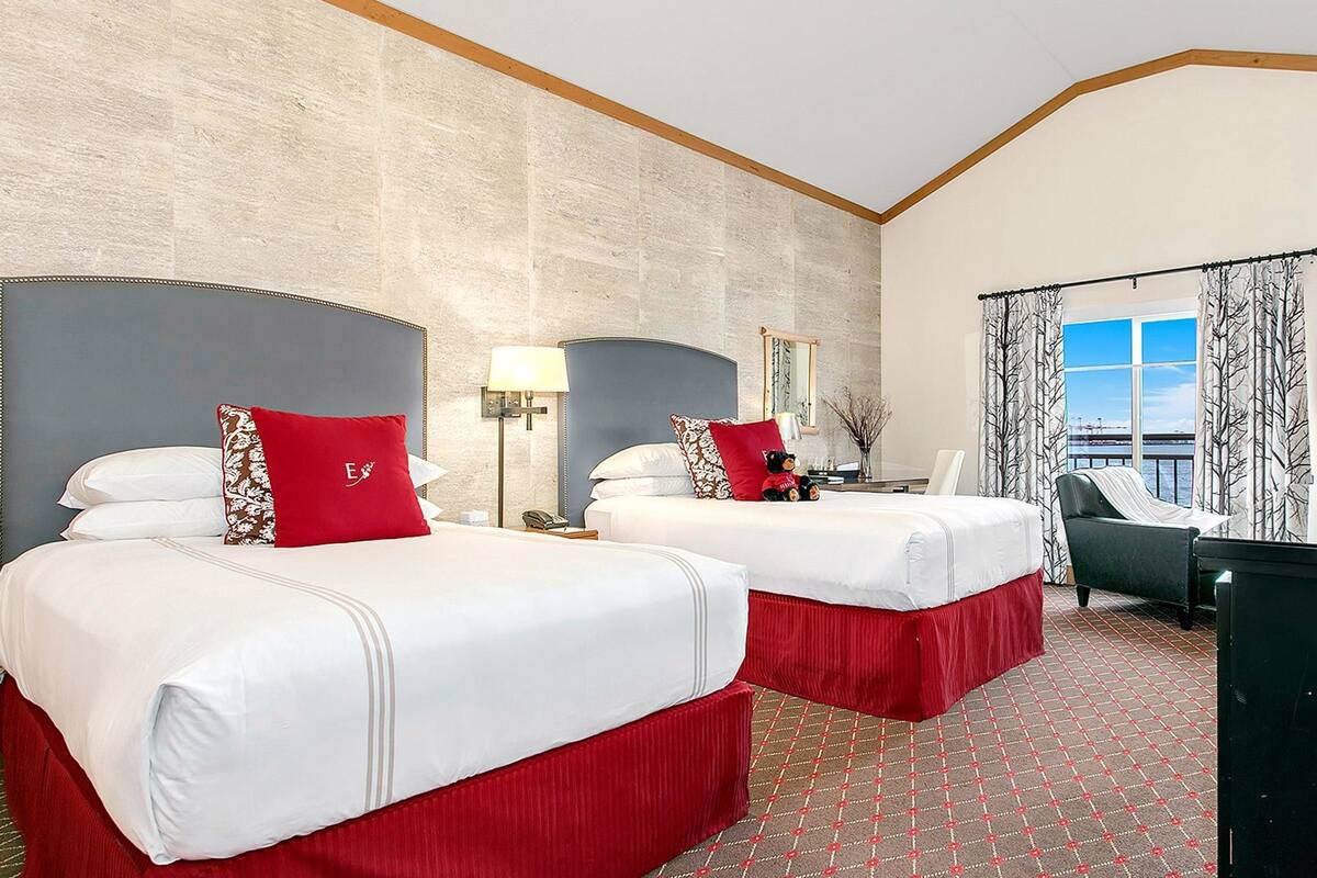 A hotel room with two beds, a desk, a chair, and a view of the water.