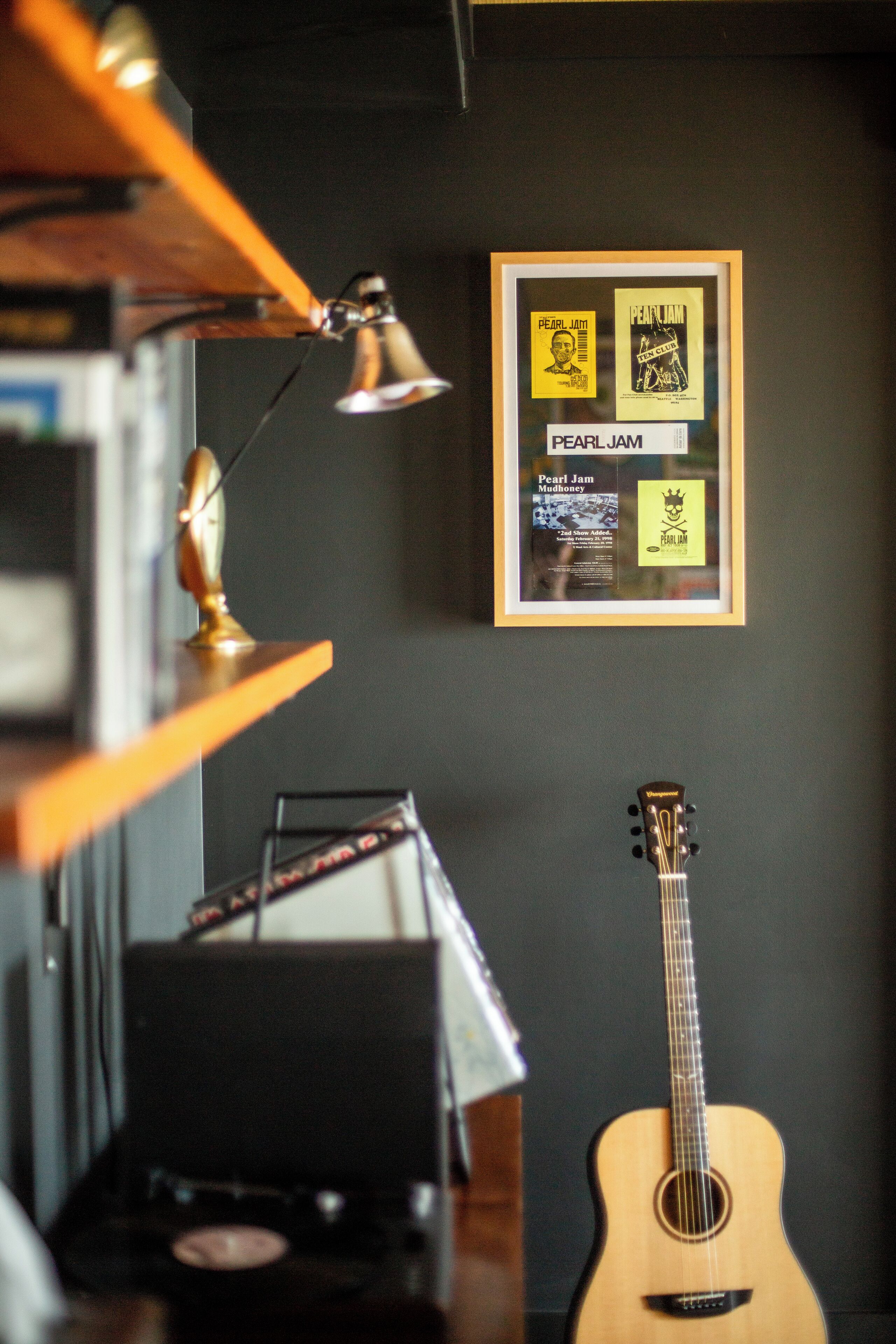 A framed poster of Pearl Jam on a dark wall, a guitar, and a record player.