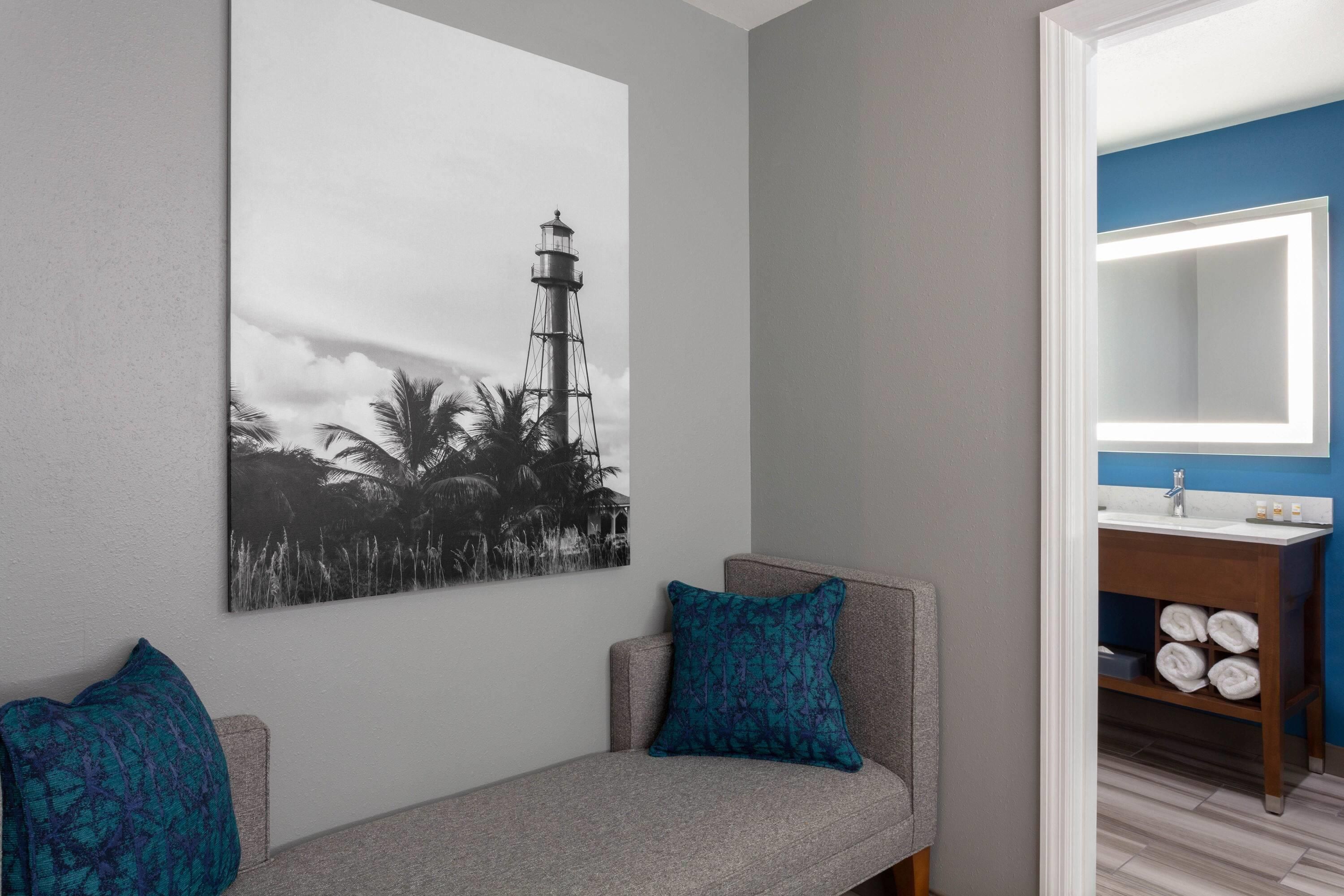 Una habitación con sofá gris, un cuadro colgado en la pared de un faro y un baño con pared azul y tocador de madera.