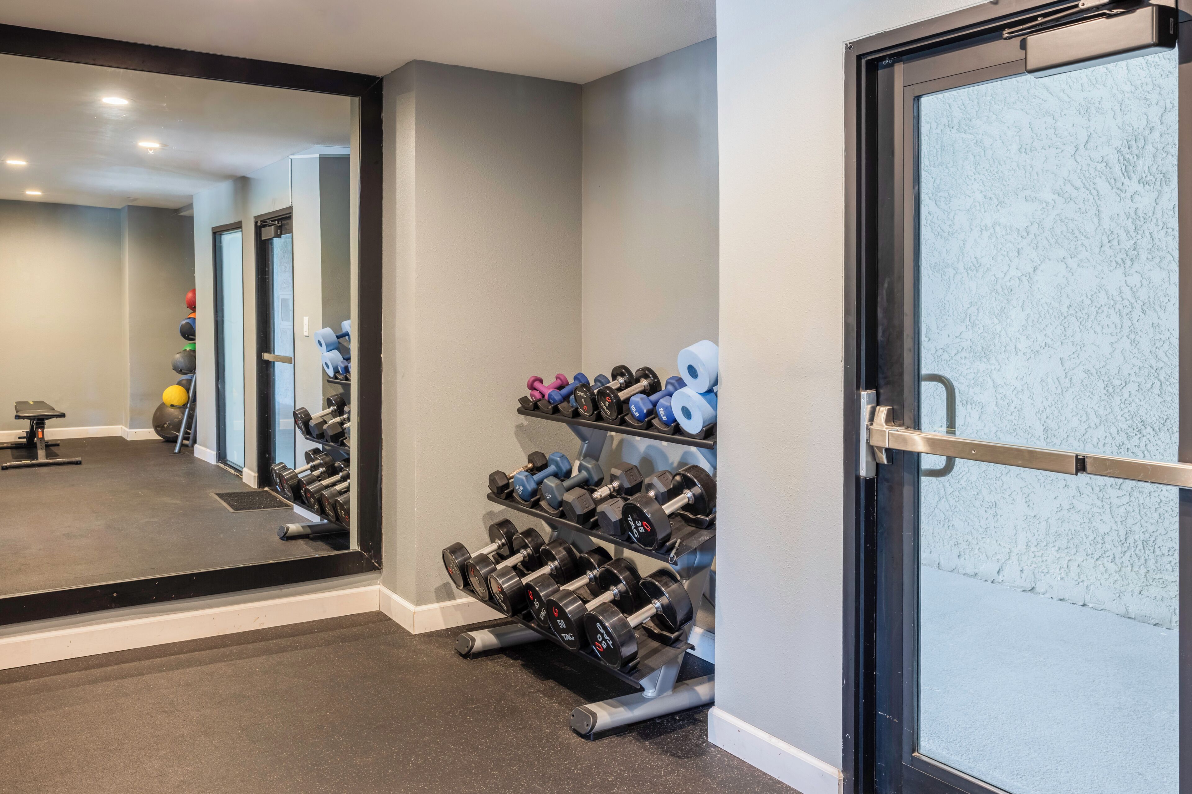 Ett gym med träningsredskap, en bänk och en spegel som reflekterar rummet.