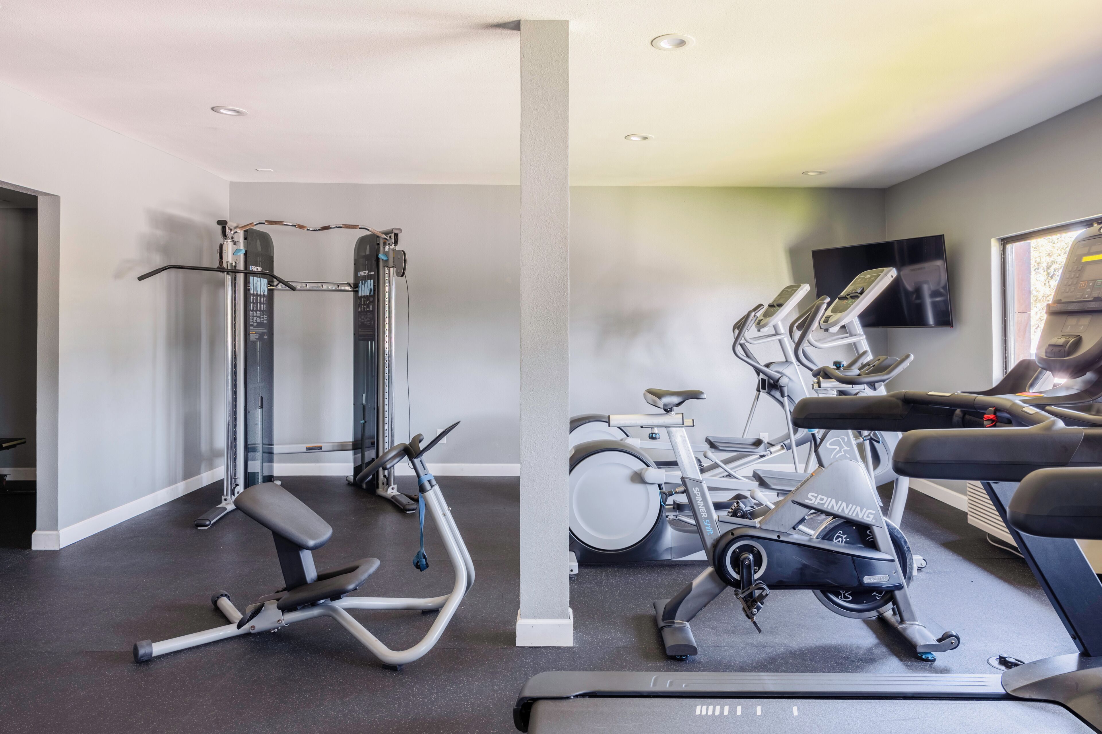 Un gimnasio en casa con barra de dominadas, banca de pesas, bicicleta estática y cinta de correr.