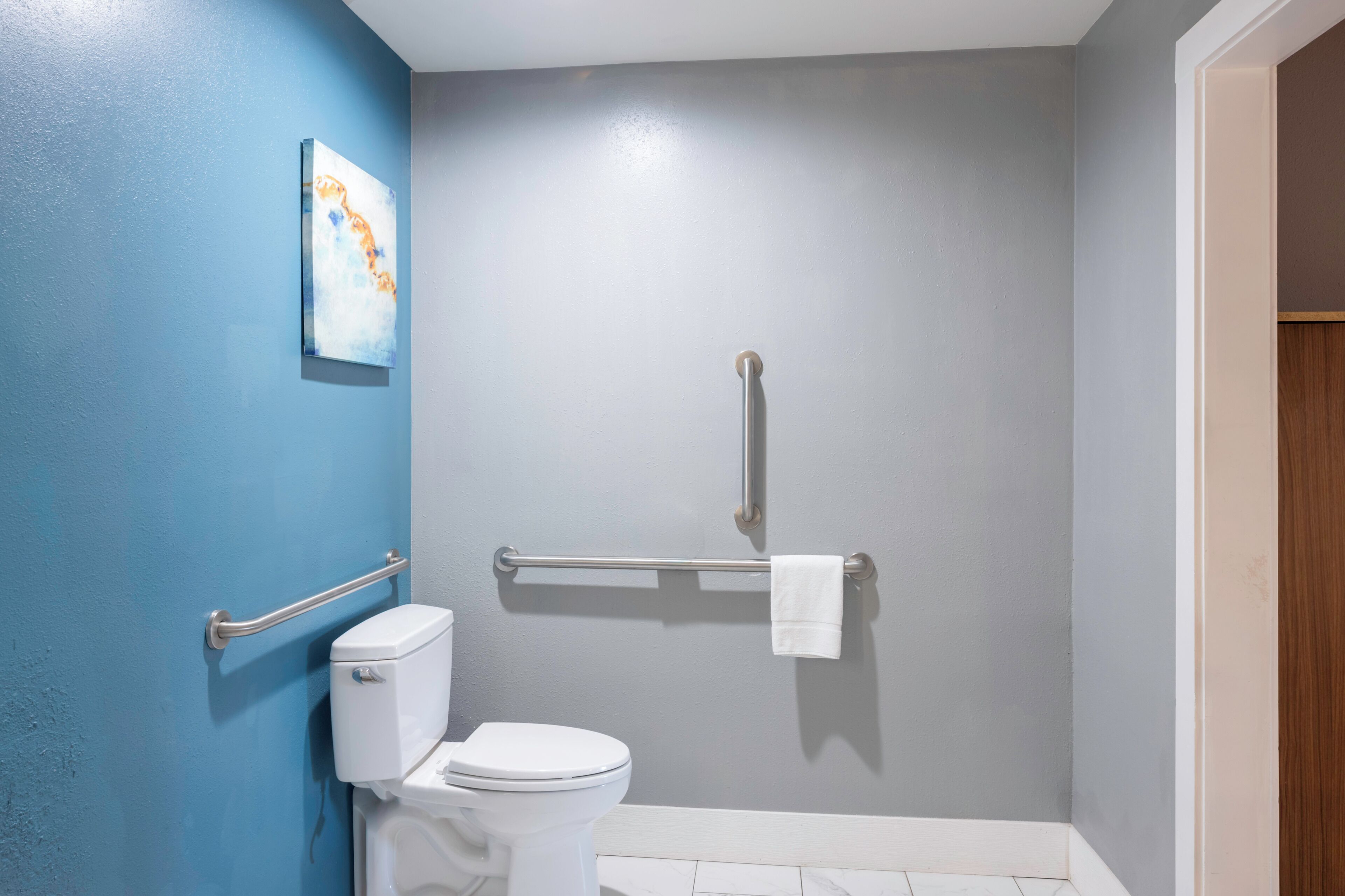 A bathroom with a blue wall, a white toilet, a grab bar, and a towel rack.