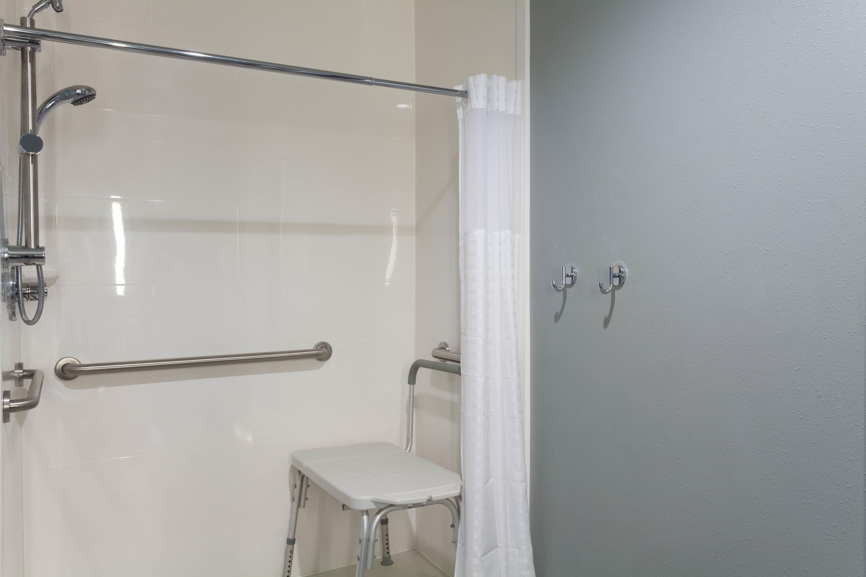 Une salle de bain équipée d’une douche, de barres d’appui, d’un banc blanc et d’une porte dotée d’une poignée.