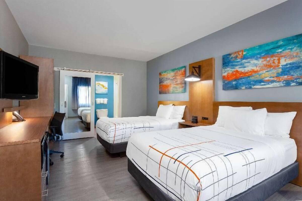 Una habitación de hotel con dos camas, un escritorio con televisor y obras de arte en las paredes.