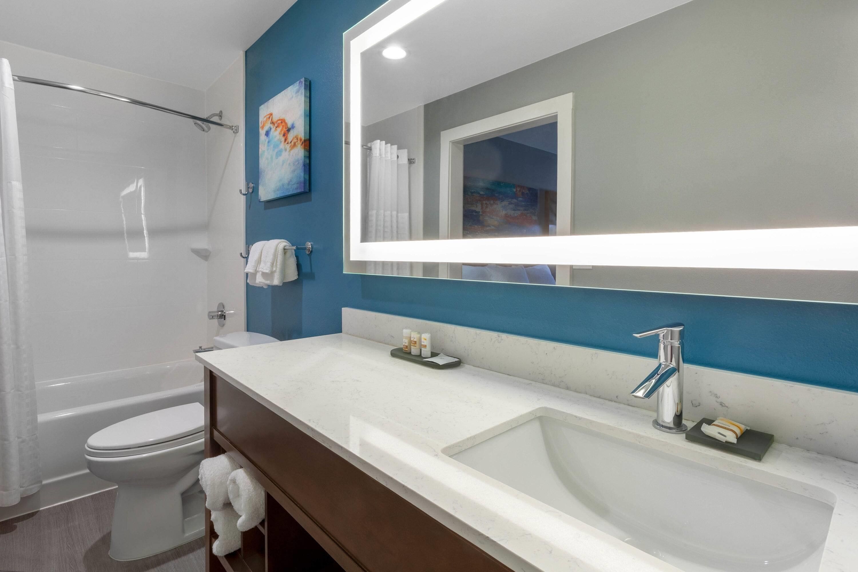 A modern bathroom with a bathtub, toilet, and a large mirror above the sink.