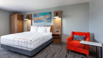 Una habitación de hotel con una cama, un sillón rojo, una mesita y un cuadro en la pared.