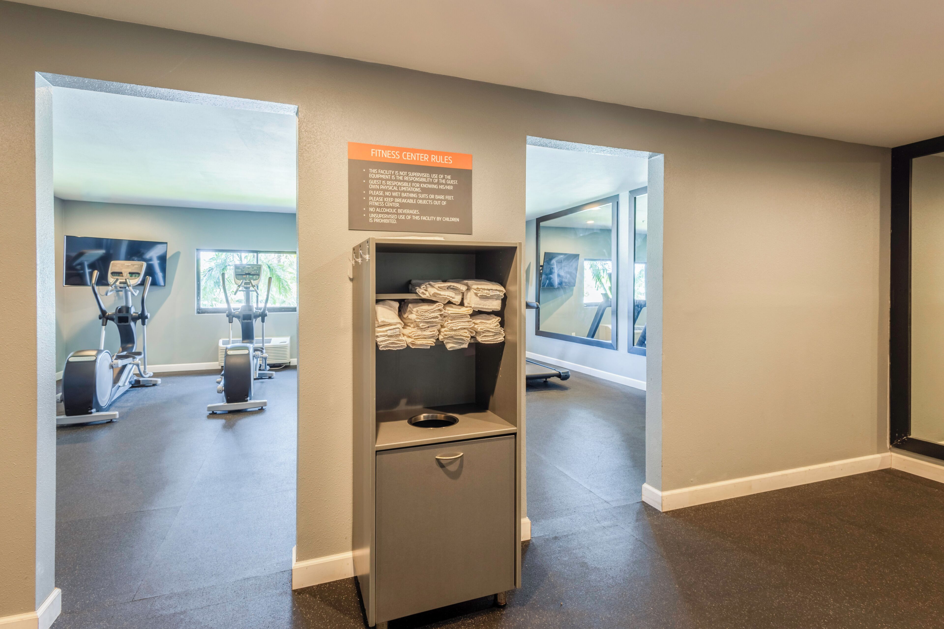 Une salle de sport équipée de matériel d’exercice, d’un porte-serviettes et d’un panneau indiquant les règles à respecter.