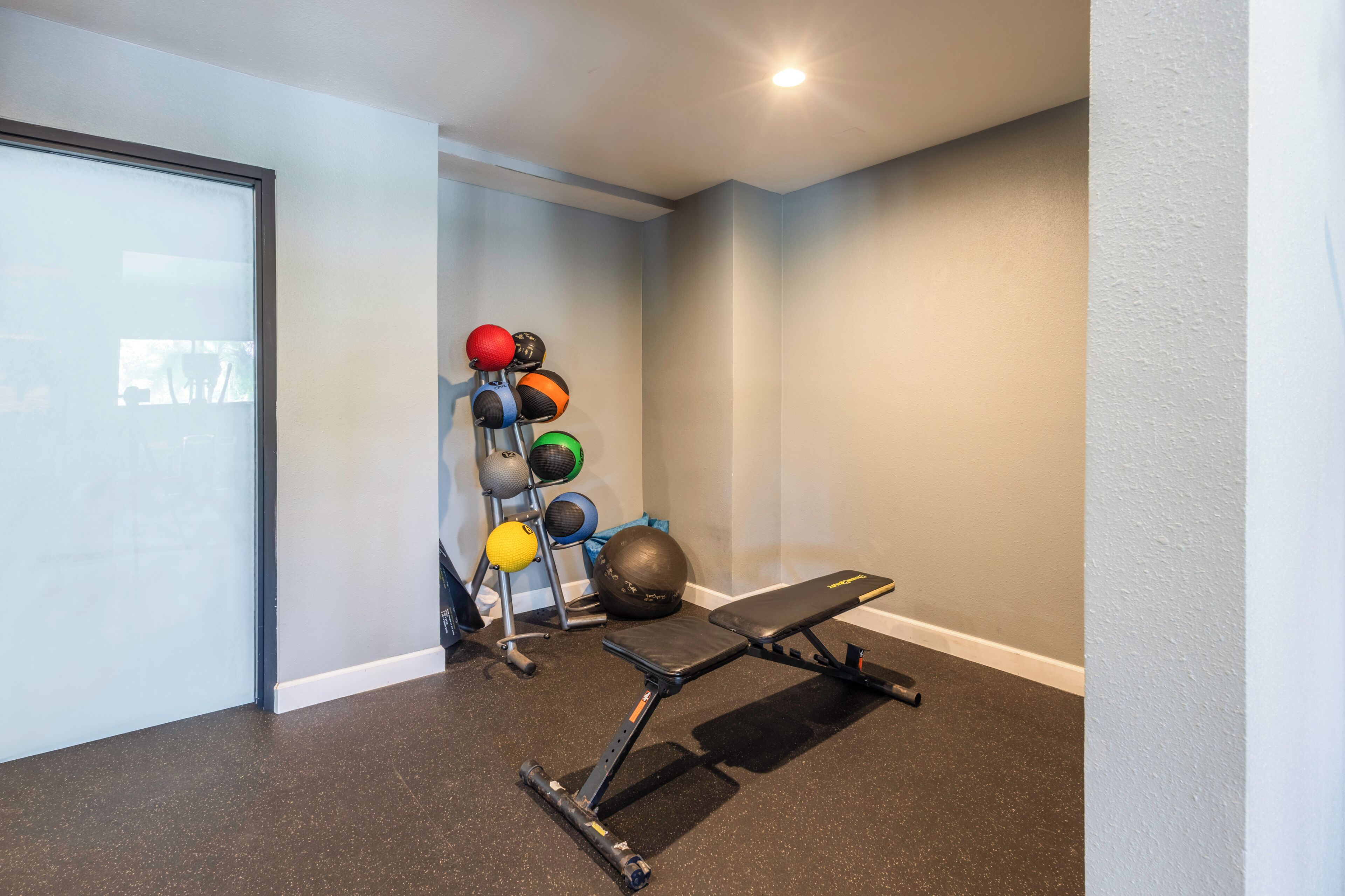 A home gym with a bench, a wall-mounted medicine ball rack, and a weight bench.