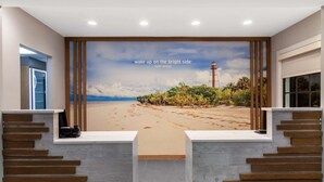 Un área de recepción con un mural de vistas a la playa, una escalera y un mostrador de recepción.