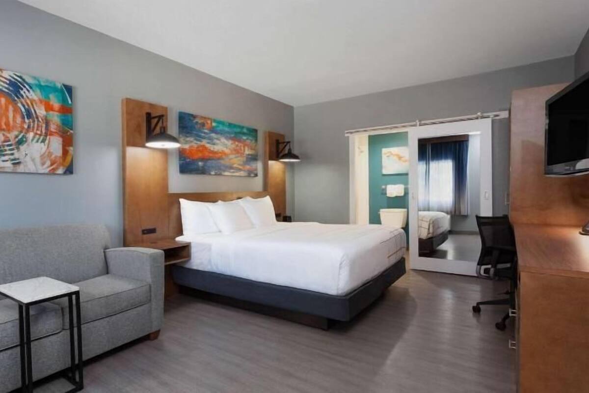 Habitación de hotel con cama, sofá, escritorio, televisión y obras de arte en las paredes.