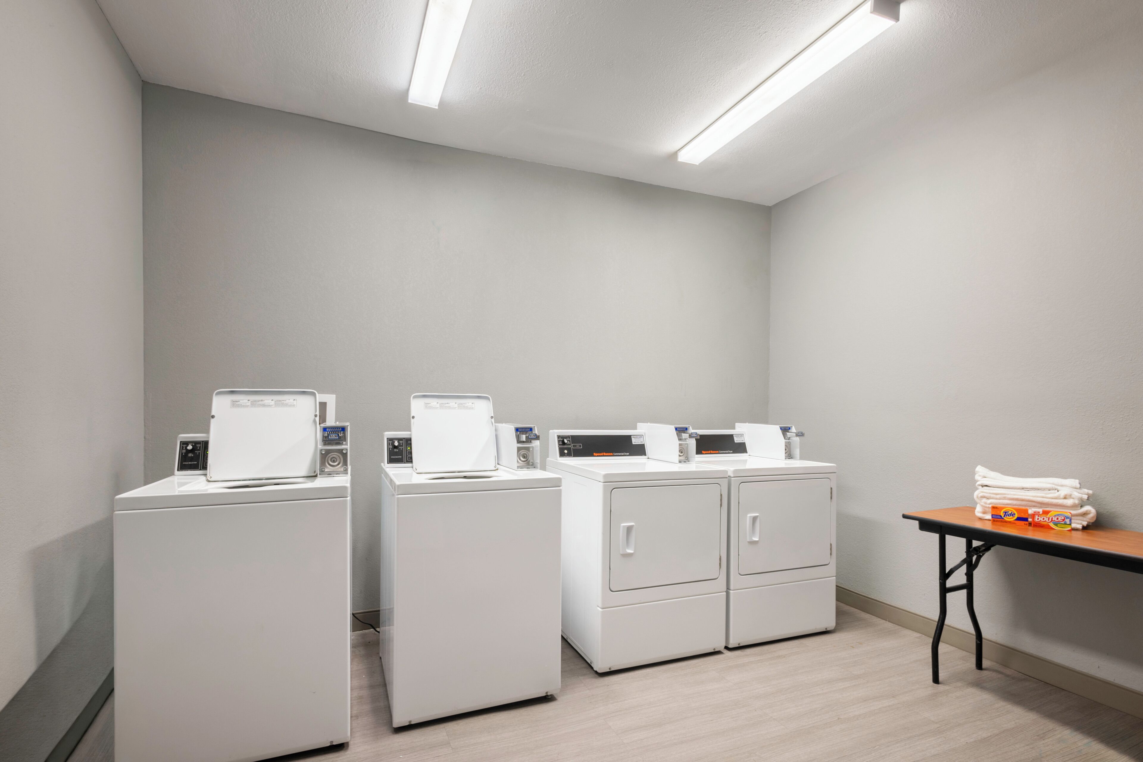 A laundry room with four white washing machines, a table with folded towels, and a ceiling light fixture.