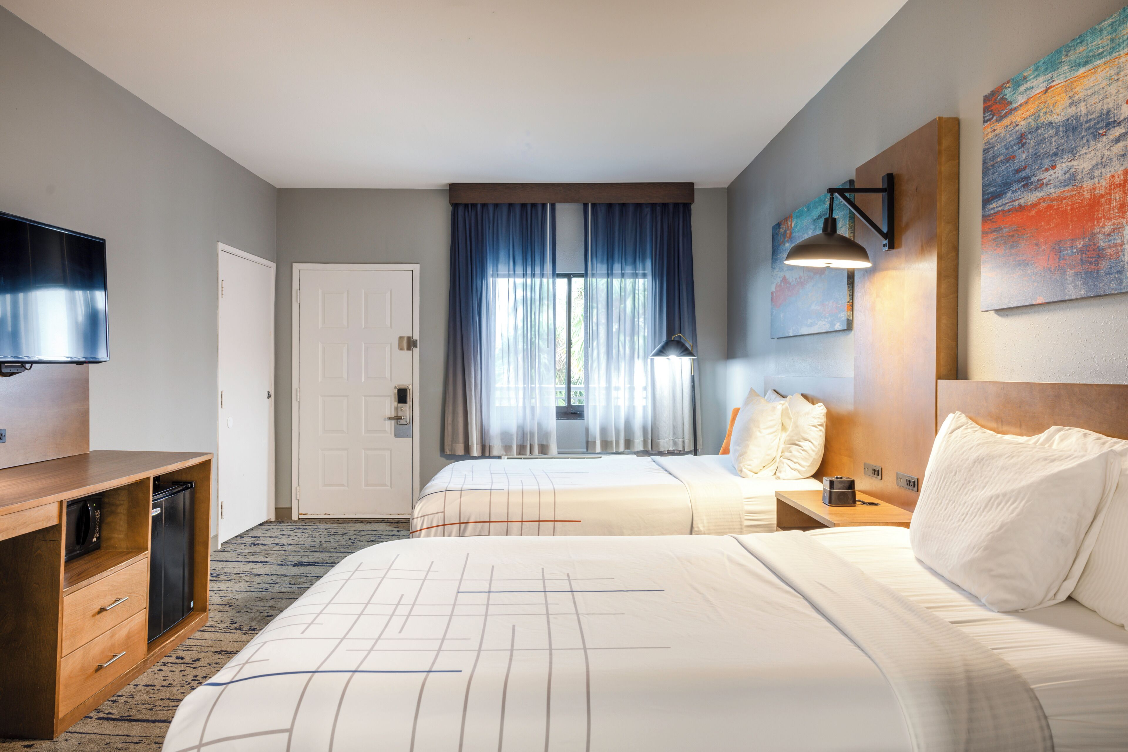 Une chambre d’hôtel avec deux lits, une télévision, un bureau et une fenêtre avec des rideaux.