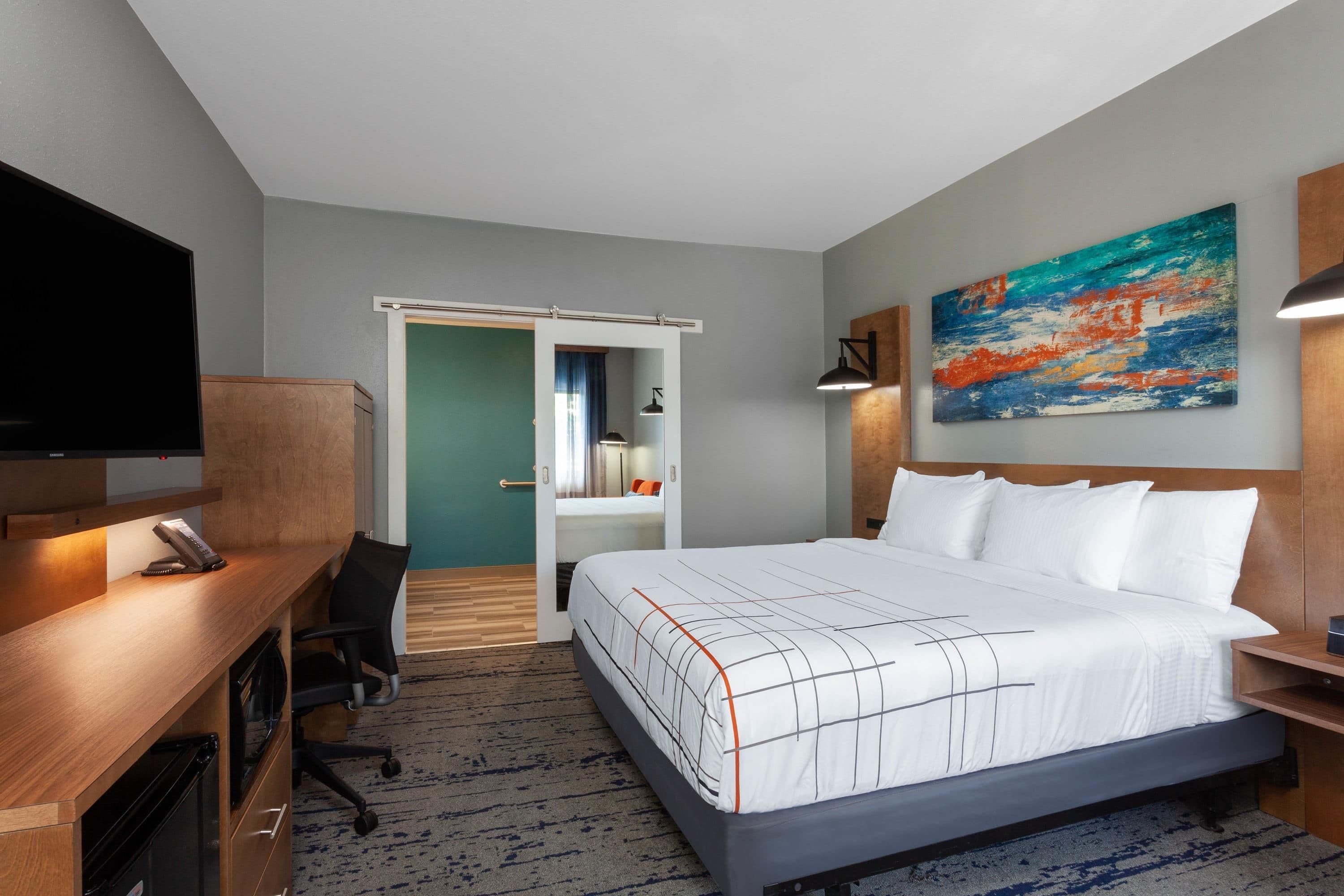 Ein Hotelzimmer mit Bett, Schreibtisch, Stuhl, Fernseher und Kunstwerken.