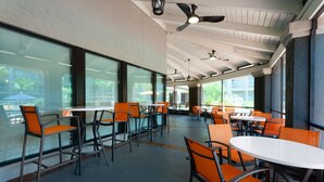 Un amplio comedor interior con techos altos, ventanas grandes, sillas naranjas modernas y mesas blancas.