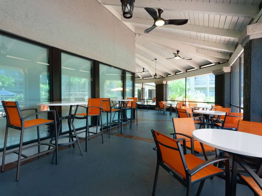 A spacious indoor dining area with high ceilings, large windows, and modern orange chairs and white tables.