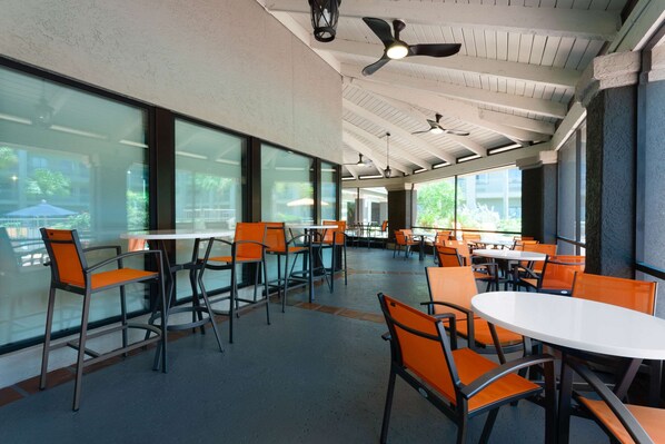 Un amplio comedor interior con techos altos, ventanas grandes, sillas naranjas modernas y mesas blancas.