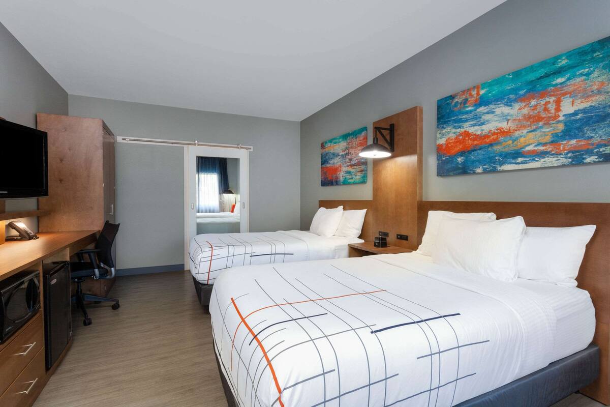 Una habitación de hotel con dos camas, un escritorio, un televisor y obras de arte en las paredes.