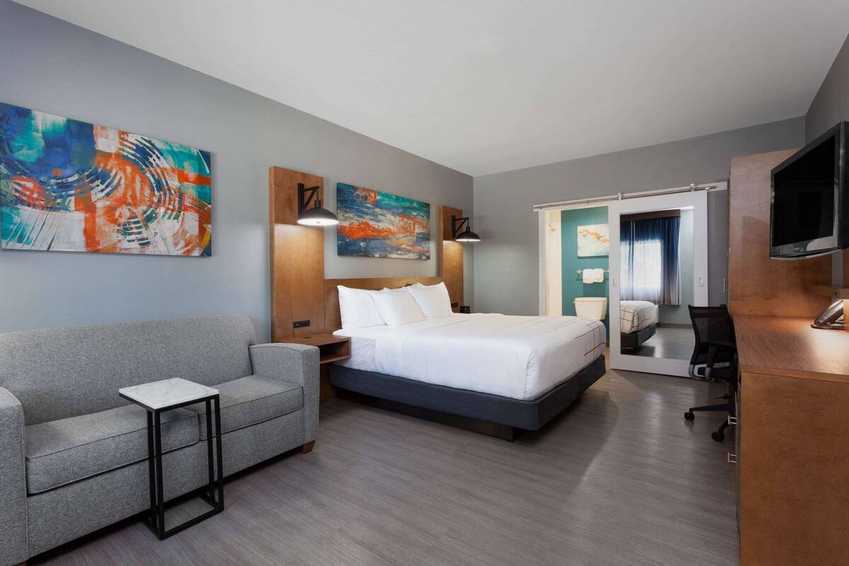Una habitación de hotel moderna con una cama, un sofá, una mesita, un escritorio y un televisor.