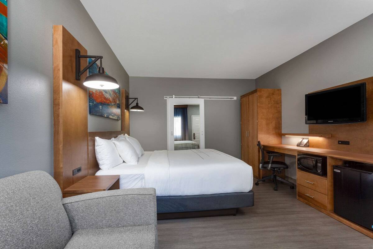 Una habitación de hotel pequeña con cama, escritorio, silla, televisión y microondas.