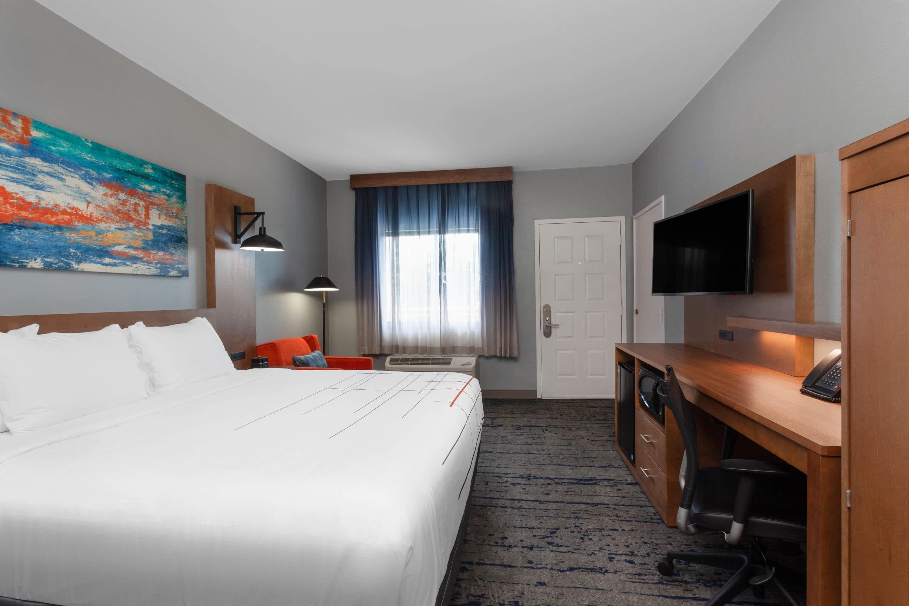 A hotel room with a large bed, a desk, a television, and a painting on the wall.
