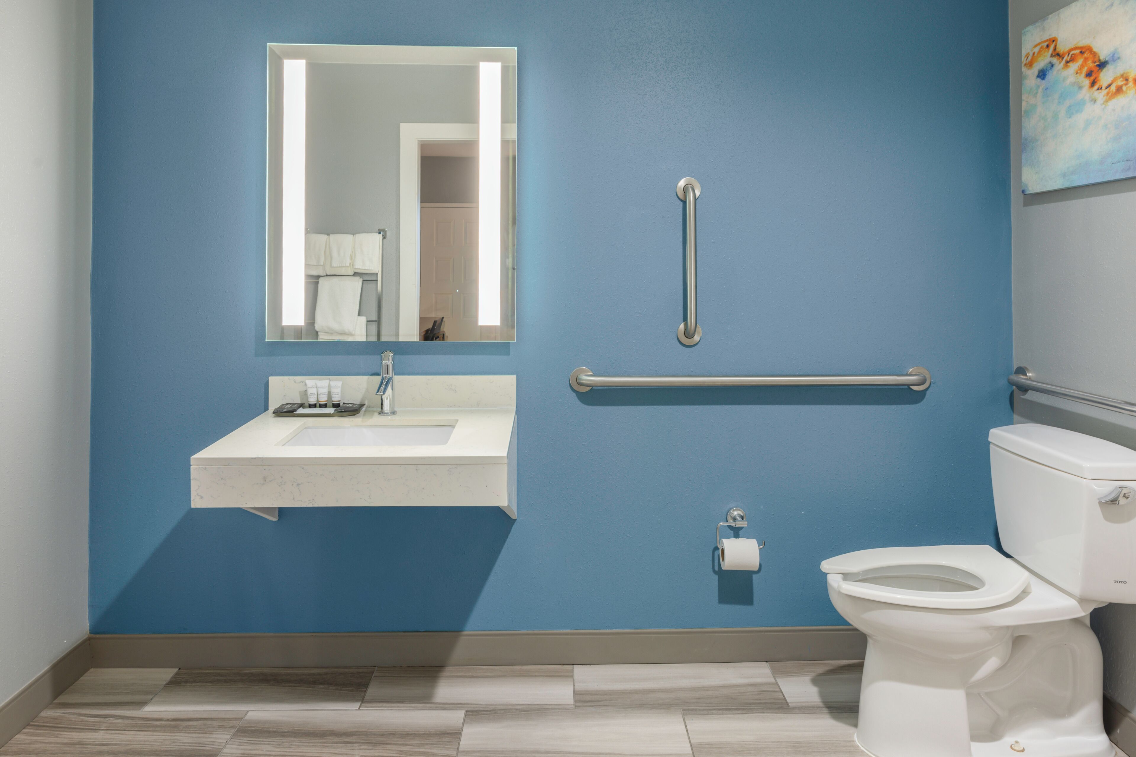 A bathroom with a blue wall, a white sink, a mirror, a toilet, and a handrail.