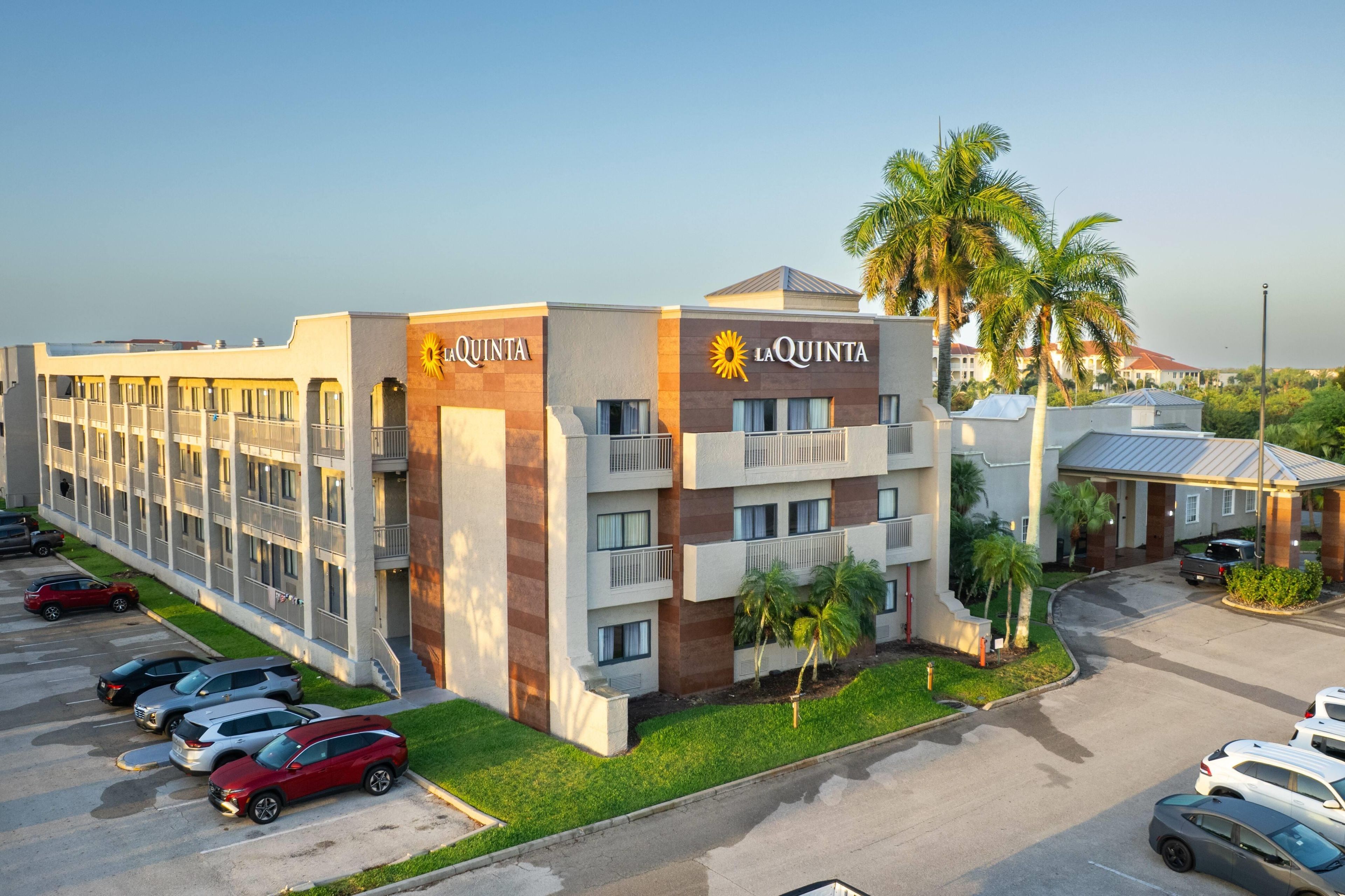 Un hôtel au design moderne, reconnaissable à son grand panneau « La Quinta », doté de nombreux balcons et disposant d’un parking où sont stationnées plusieurs voitures.