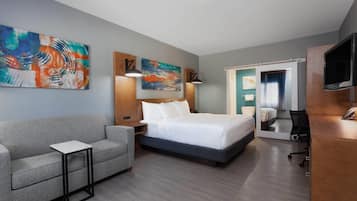 Habitación de hotel con cama, sofá, escritorio y obras de arte en las paredes.