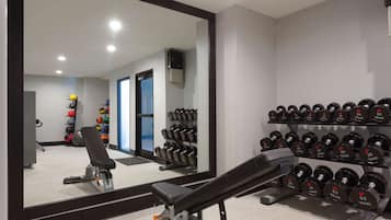 Un gimnasio con una prensa de banca, mancuernas y un espejo que refleja el espacio.