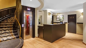 A hotel reception area with a modern design, including a reception desk, a staircase with patterned carpet, and a door marked "HOTEL". - Best Western Plus Hôtel de Dieppe 1880 (Rouen)