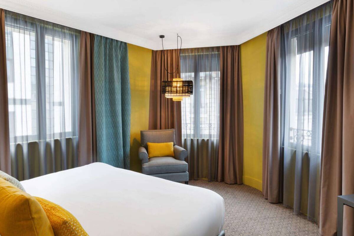 Een hotelkamer met een groot bed, een stoel, een televisie en gordijnen.