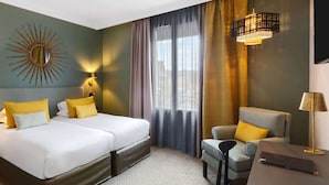 A hotel room with two beds, a sofa, a chair, a TV, and a sunburst mirror on the wall. - Best Western Plus Hôtel de Dieppe 1880 (Rouen)