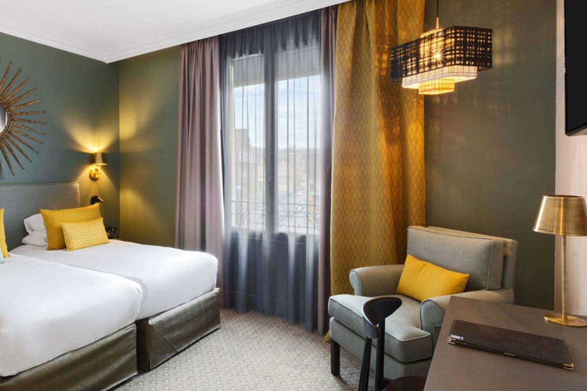 Een hotelkamer met twee bedden, een bank, een stoel, een televisie en een spiegel met zonnestralen aan de muur.