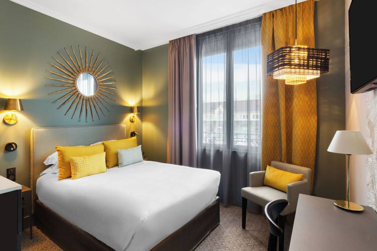 Een hotelkamer met een groot bed, een bureau, een stoel, een televisie en een raam met gordijnen.