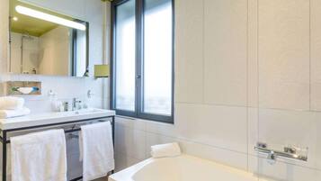 A modern bathroom with a large mirror, a bathtub, and a window.