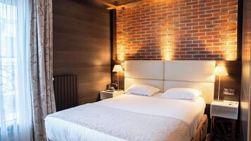 Una habitación de hotel con una cama grande, cabecera de madera, dos mesitas de noche con lámparas y una pared de ladrillo.