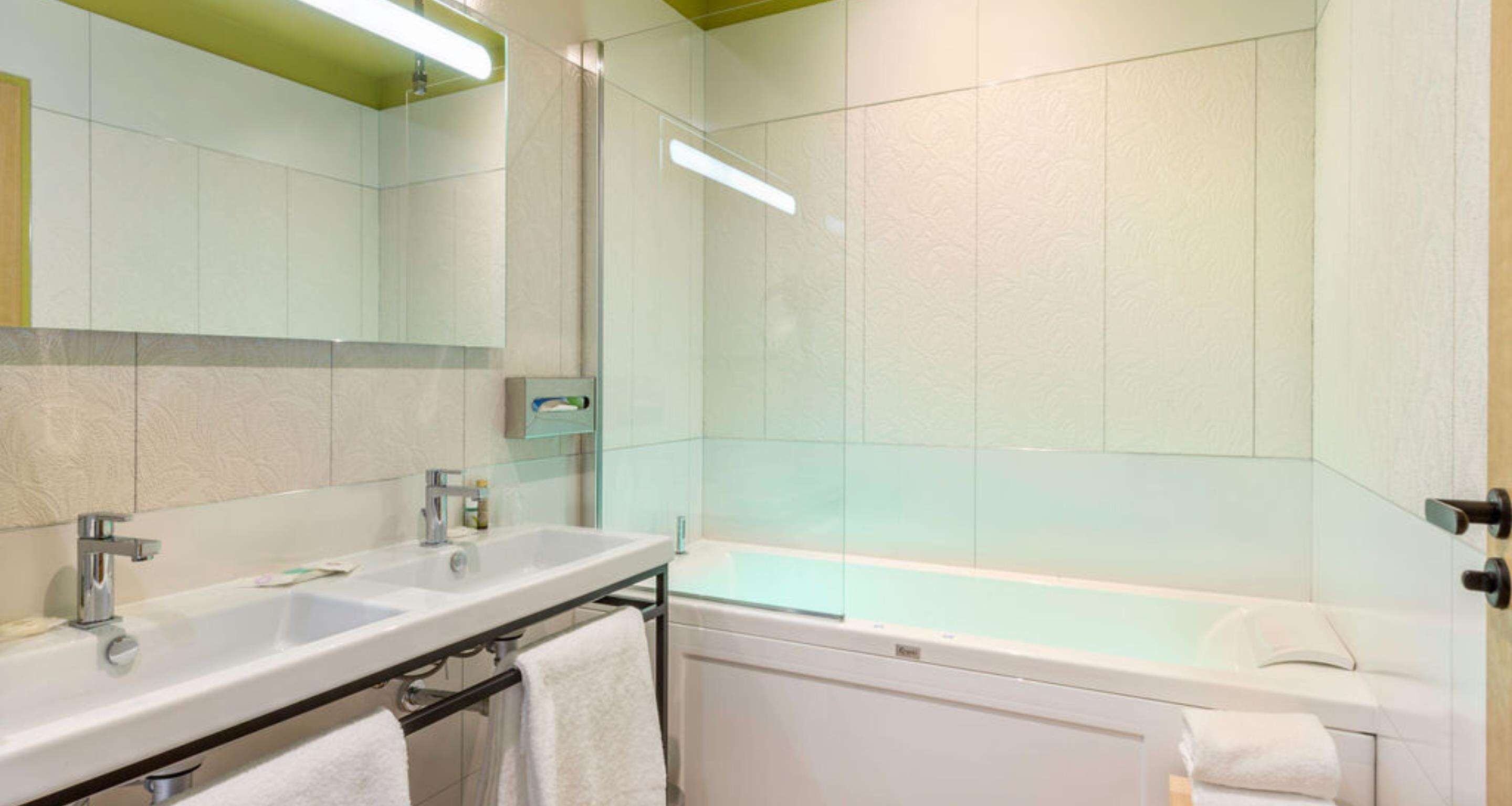 Un baño moderno con tocador de doble lavabo, ducha con mampara de vidrio y bañera independiente.