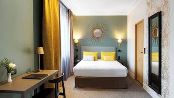 A hotel room with a bed, a desk, a chair, a lamp, and a mirror.