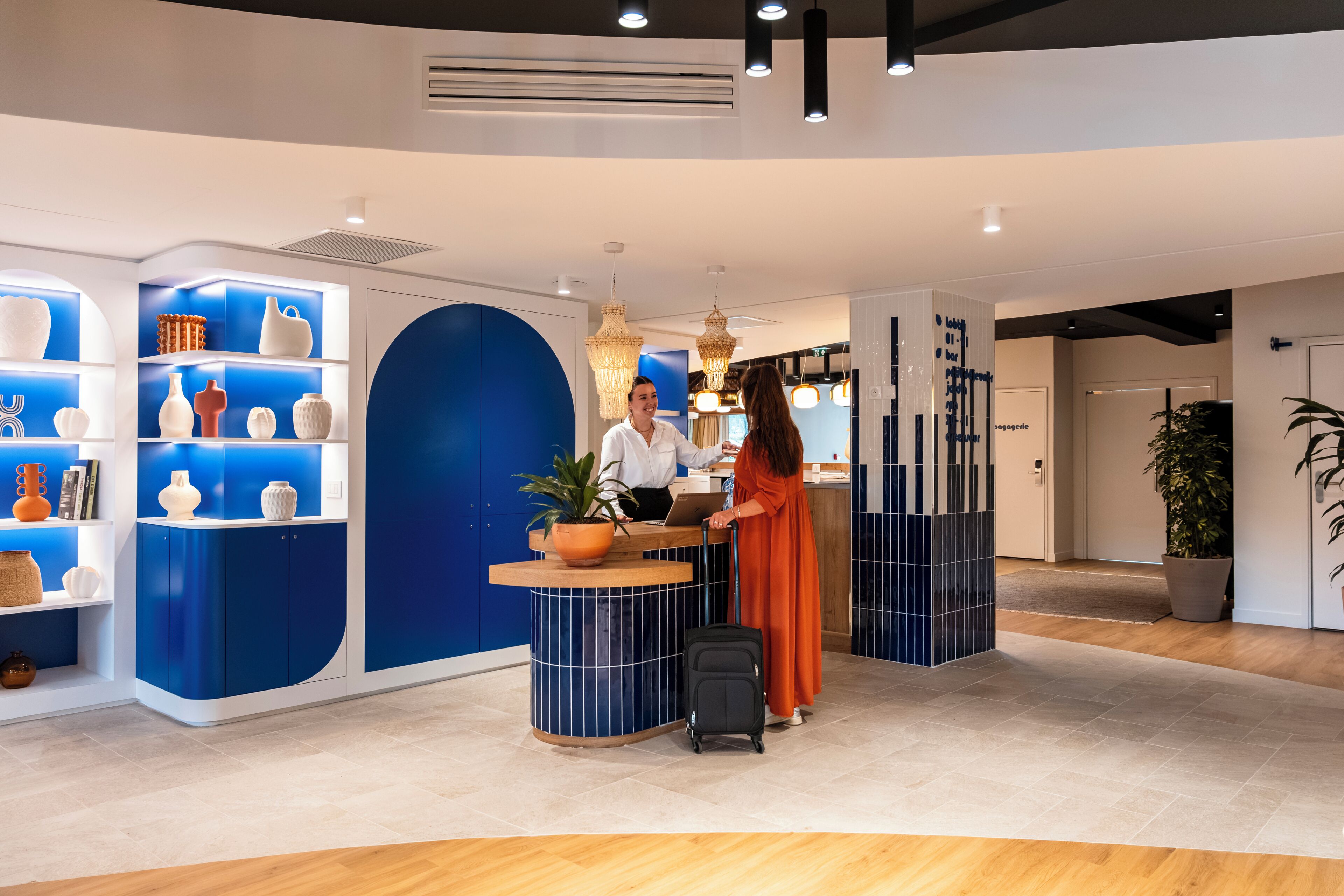 A reception desk with a blue and white color scheme, a potted plant, and a black suitcase.