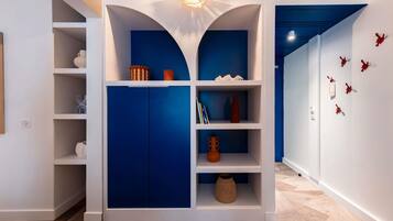 Un interior moderno con una paleta de colores azul y blanco, que incluye una estantería empotrada con objetos decorativos y una lámpara de techo original.