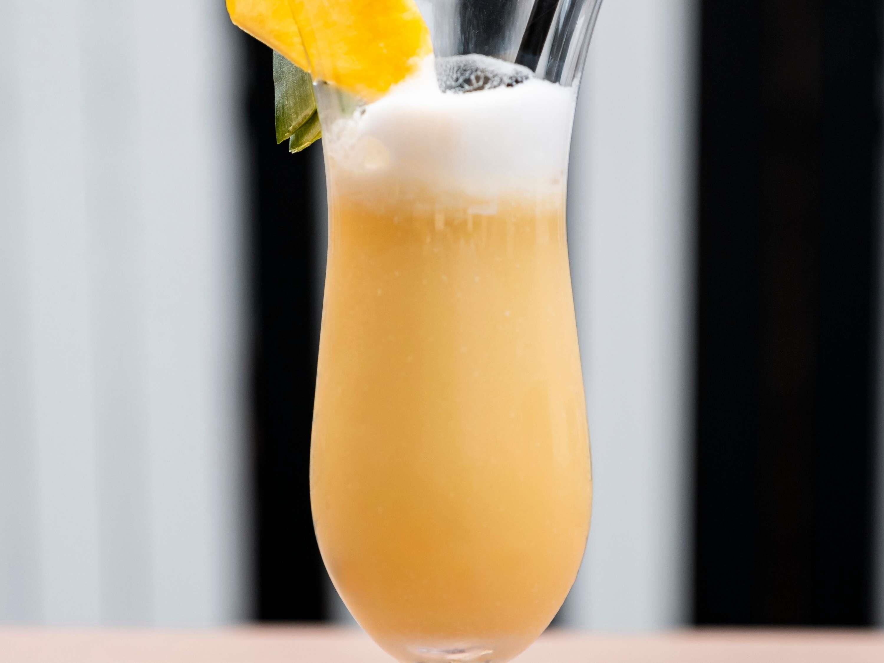 A cocktail in a tall glass with a yellow fruit garnish.