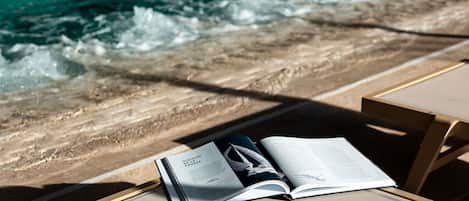 Ein Buch mit dem Titel 'Verlauf einer Krankheit' auf einem Liegestuhl am Pool, mit Wellen im Hintergrund.